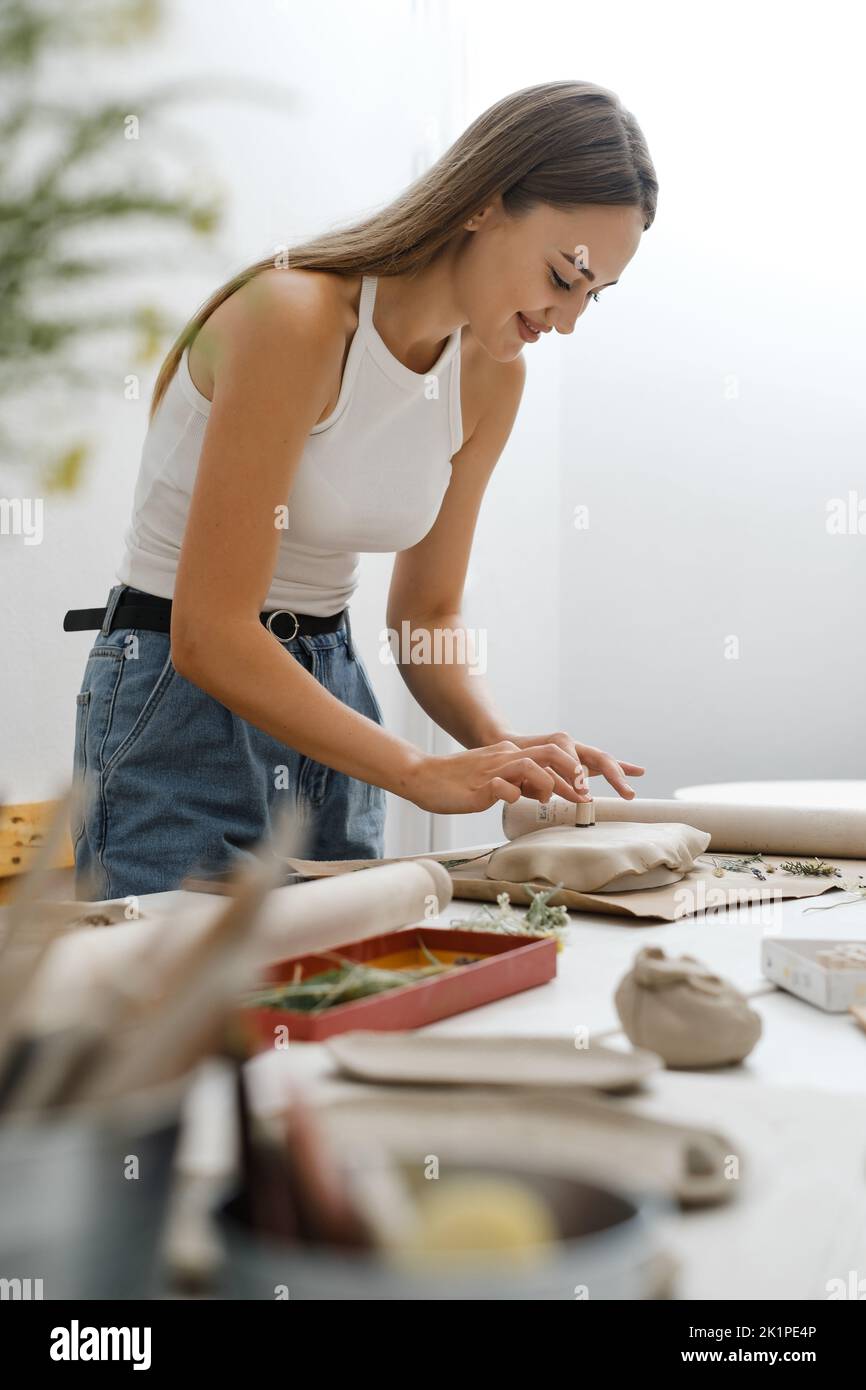 Woman rolling clay, making ceramic plate in studio with floral pattern. Handmade creative work. Pottery workshop for adults.  Stock Photo