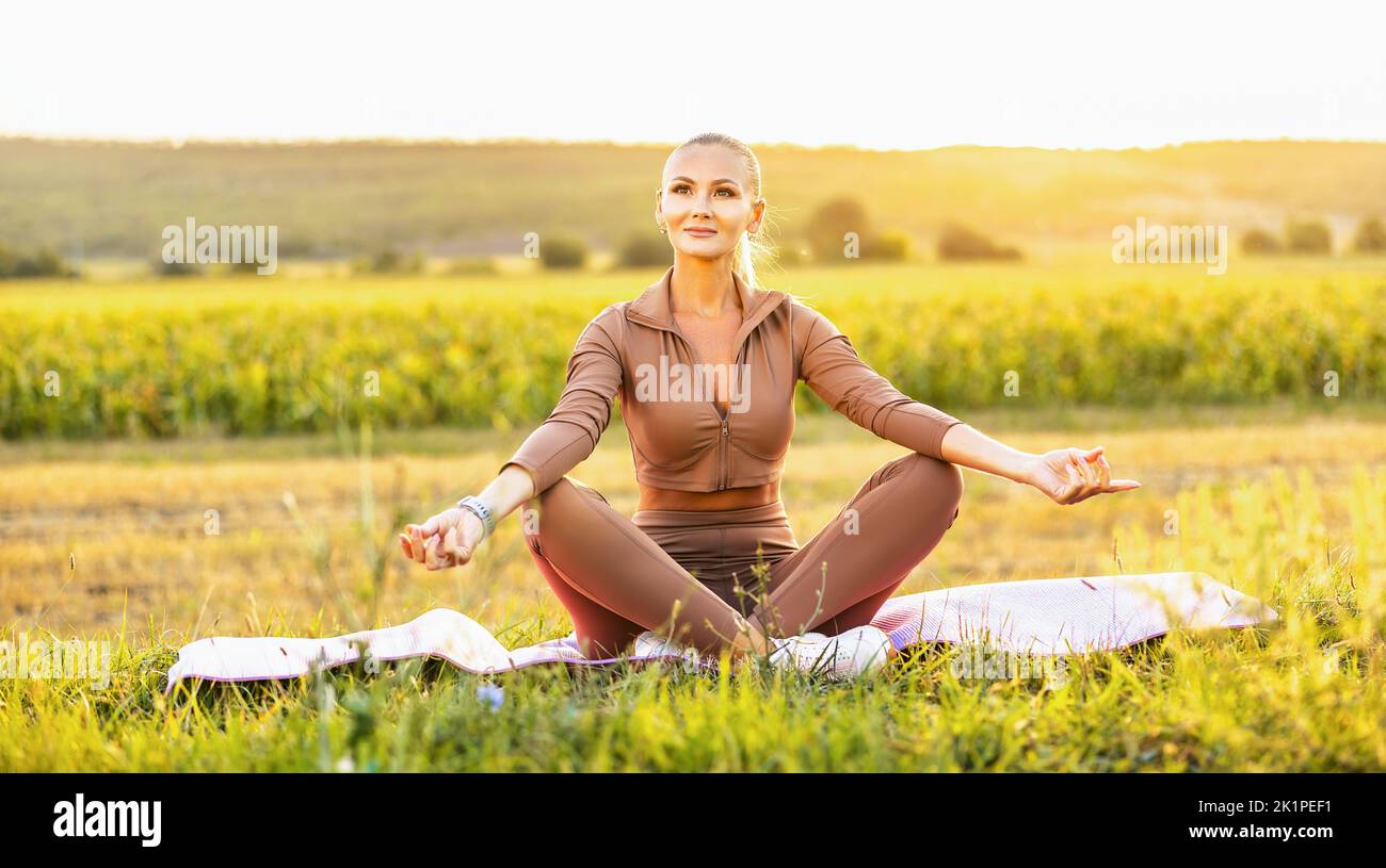 Young beautiful woman meditating in nature sitting on yoga mat and ...