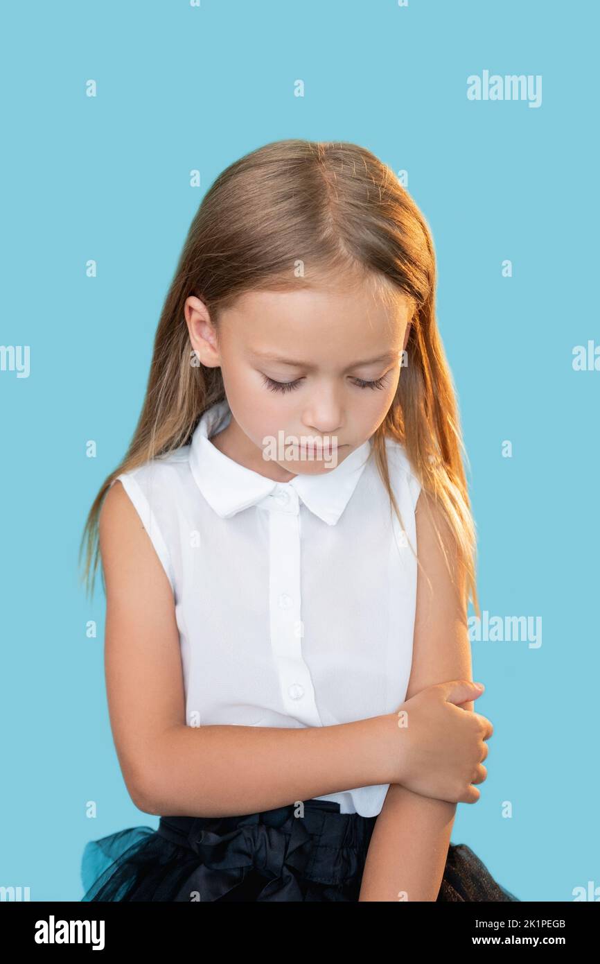 Upset girl. Kids punishment. Mistake regret. Portrait of ashamed sad little child in elegant outfit looking down isolated on blue background. Stock Photo