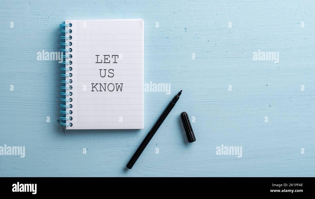 Let us know sign written in spiral notebook with a black marker next to it placed on blue wooden background. Stock Photo