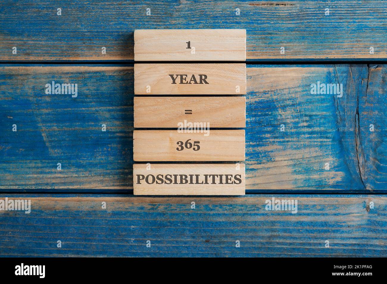 One year is 365 possibilities sign written on a stack of wooden pegs placed over blue wooden background. Stock Photo
