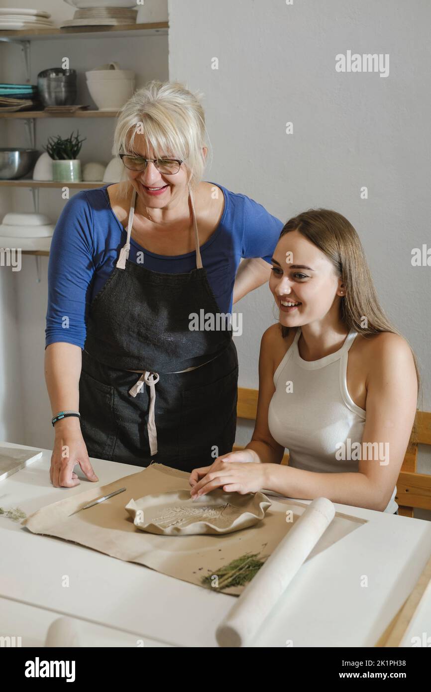 People working with clay in ceramic studio. Pottery workshop in studio. Adults learning to do ceramic plates. Pottery as hobby and leisure activity Stock Photo