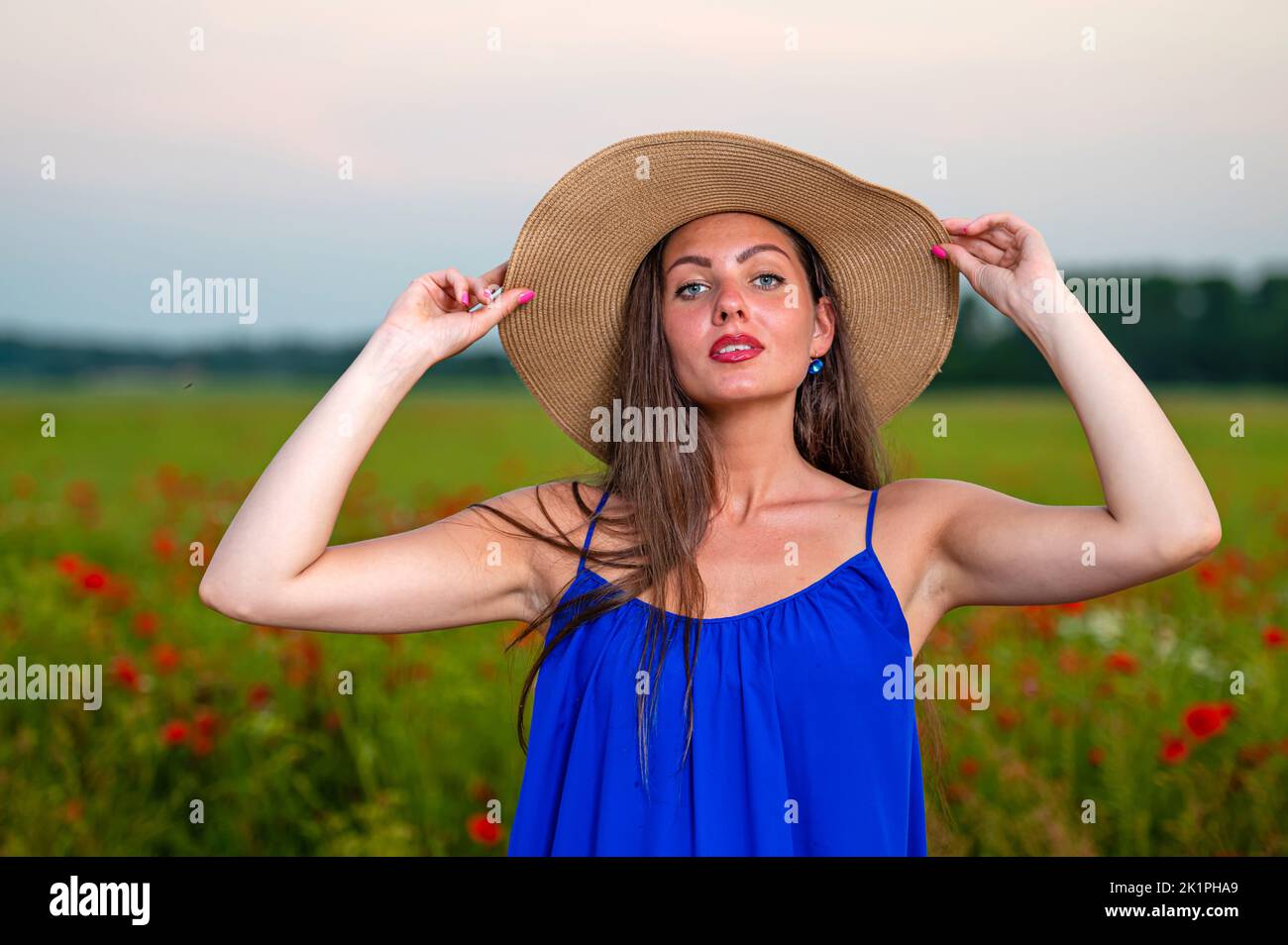 portrait of elegant young woman with long hair and straw hat in poppy ...
