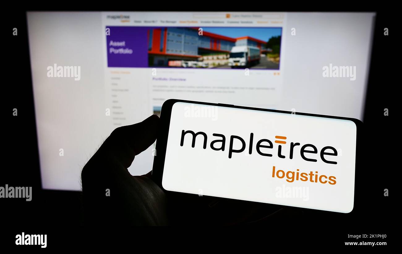 Person holding smartphone with logo of Mapletree Logistics Trust Management Ltd. (MLT) on screen in front of website. Focus on phone display. Stock Photo