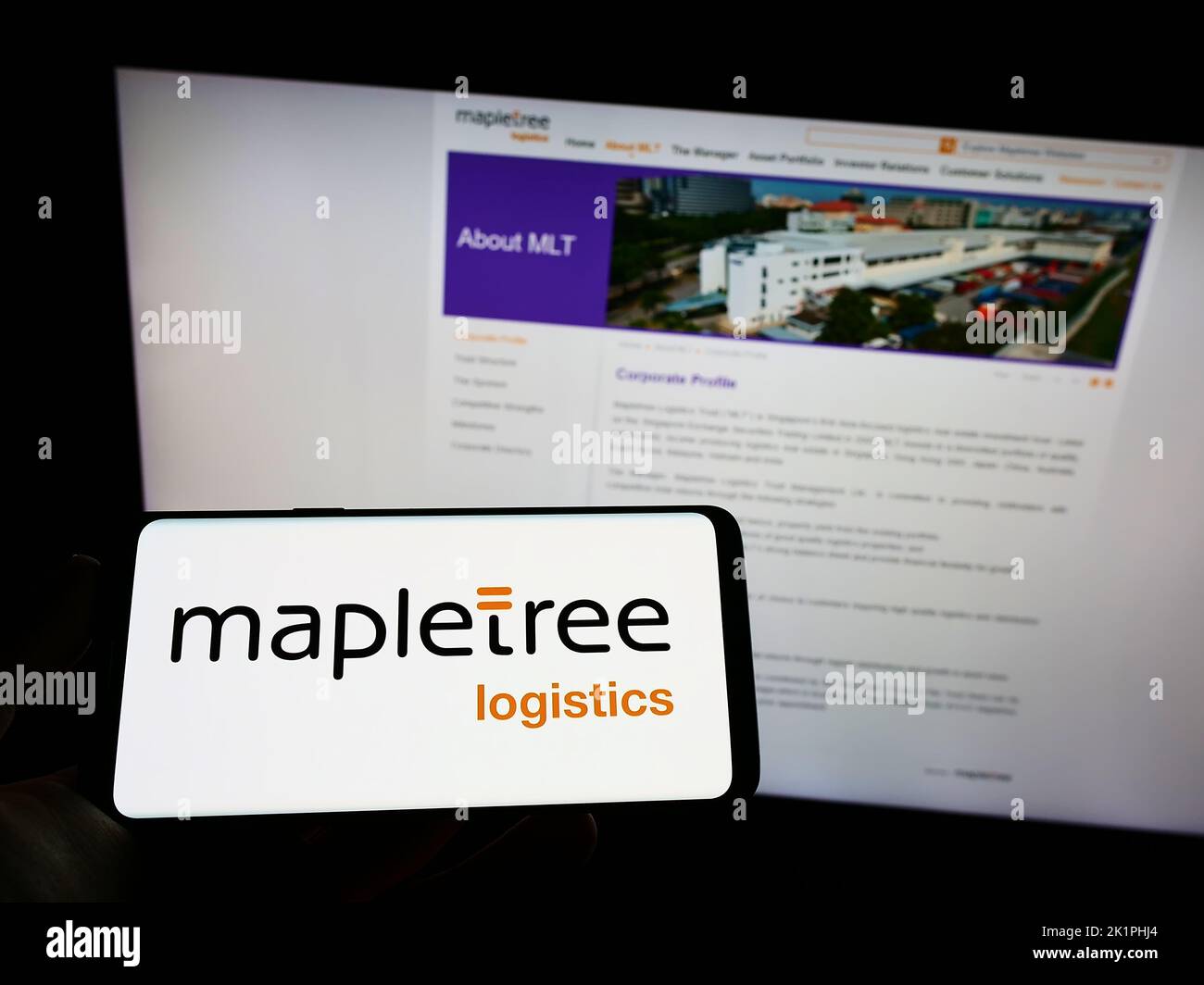 Person holding mobile phone with logo of Mapletree Logistics Trust Management Ltd. (MLT) on screen in front of web page. Focus on phone display. Stock Photo