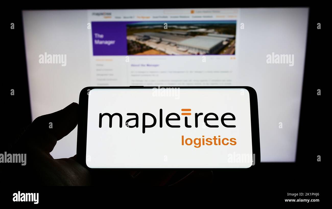 Person holding cellphone with logo of Mapletree Logistics Trust Management Ltd. (MLT) on screen in front of webpage. Focus on phone display. Stock Photo