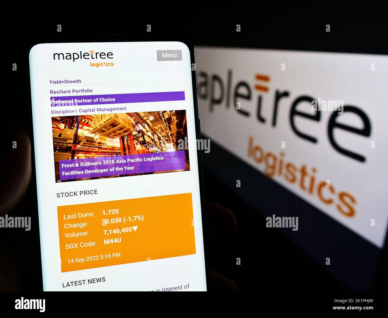 Person holding smartphone with website of Mapletree Logistics Trust Management Ltd. (MLT) on screen with logo. Focus on center of phone display. Stock Photo