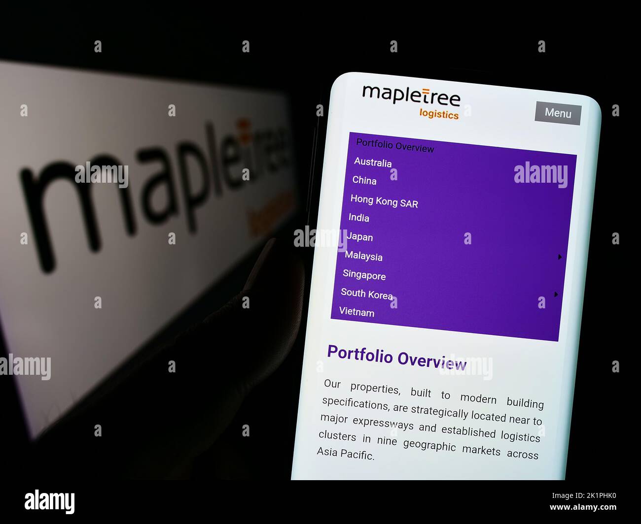 Person holding cellphone with webpage of Mapletree Logistics Trust Management Ltd. (MLT) on screen with logo. Focus on center of phone display. Stock Photo