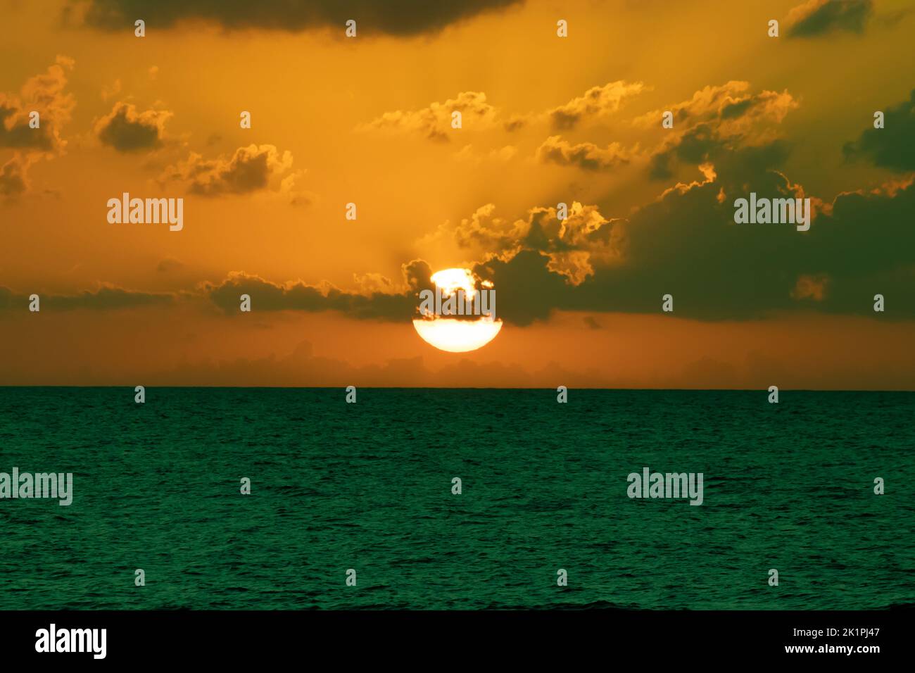 Vintage tone sunset landscape. Sun disc behind clouds. Blue sea, orange sky. End of day, elapsed time idea concept. Horizontal photo. No people. Stock Photo
