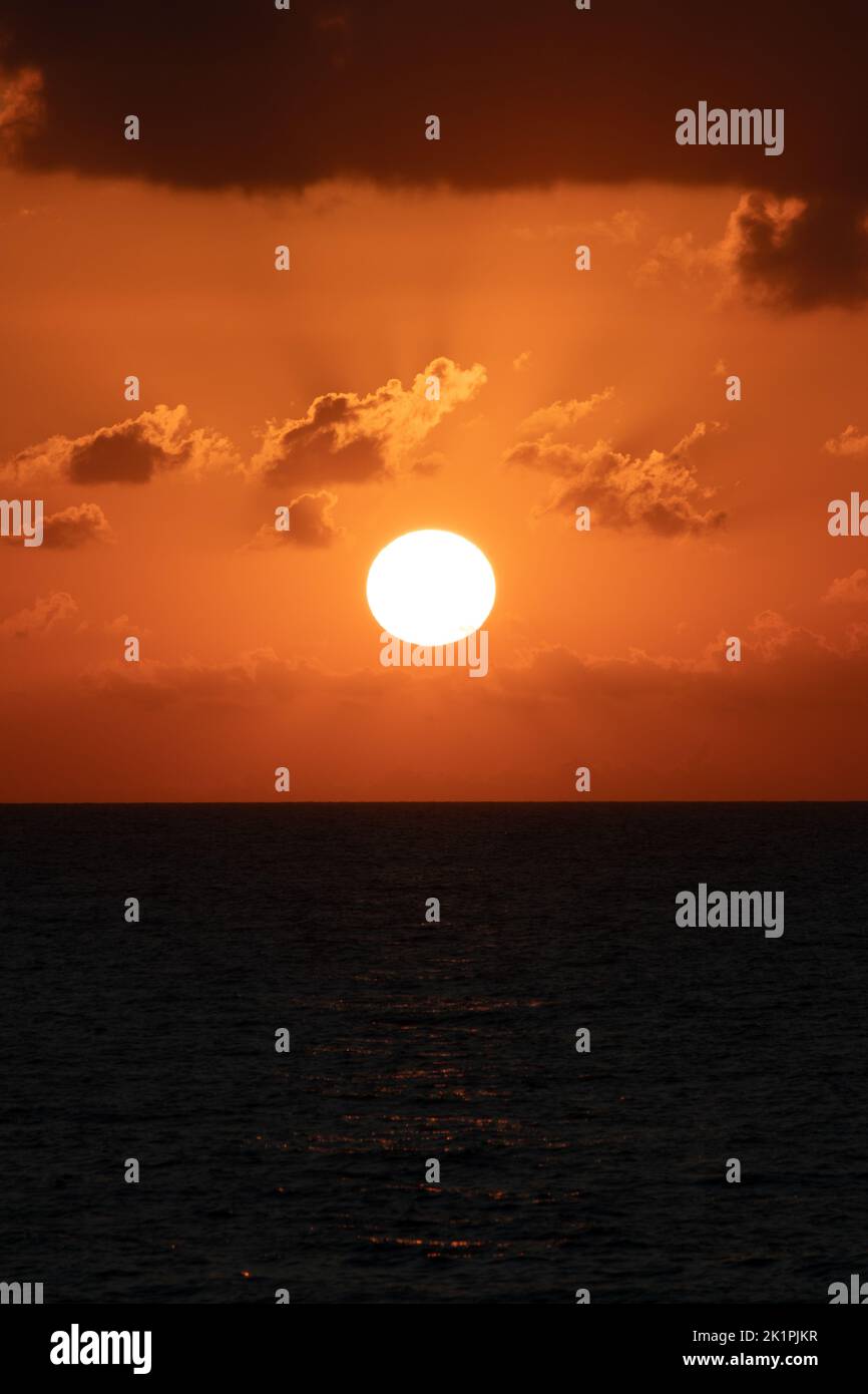 Dramatic sunset. Bright yellow sun disk and orange sky. On the dark blue sea. Vertical photo. No people, nobody. Stock Photo