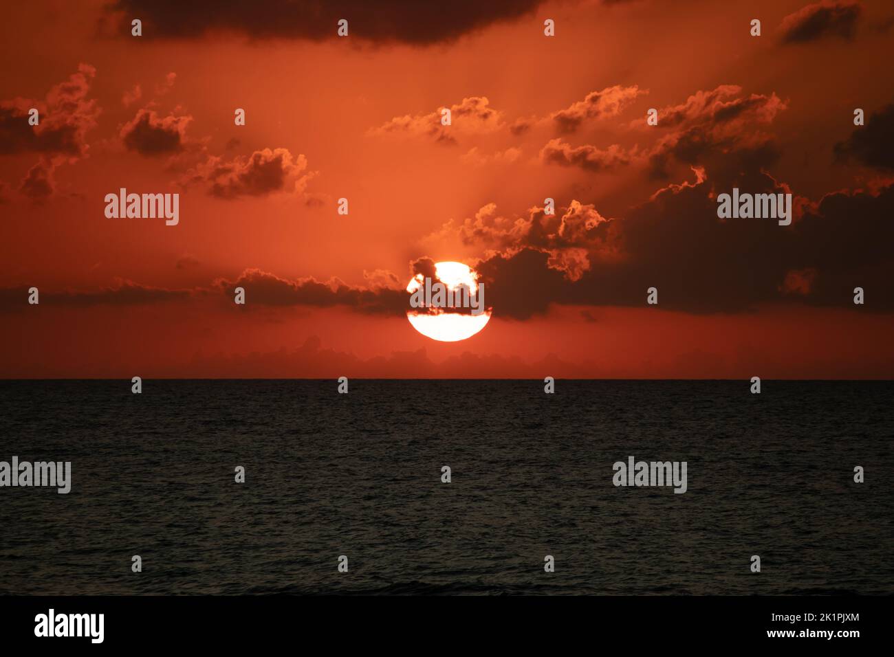 Sunset view, sunset view over the sea. Orange sky and clouds, twilight colors. The sun's bright round disk will soon disappear behind clouds. Stock Photo