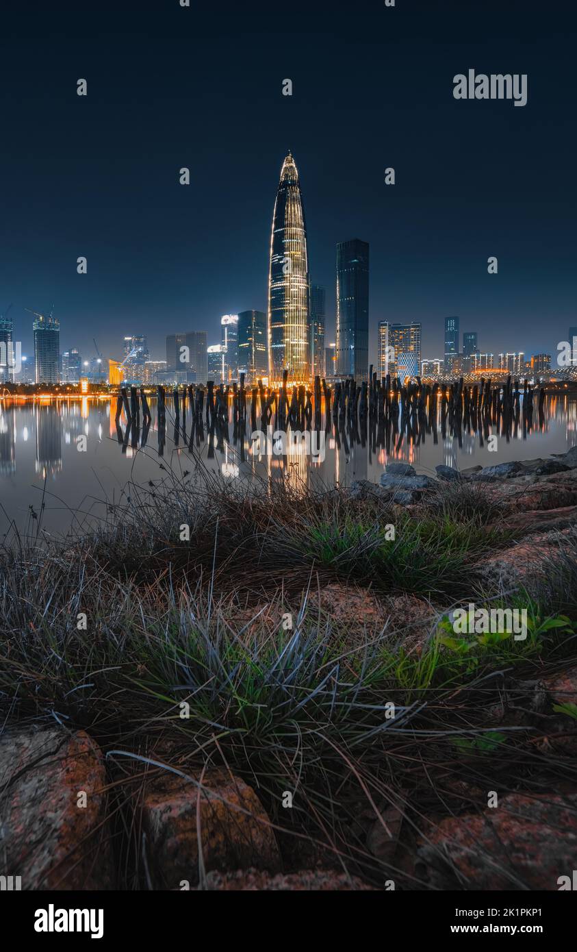 A vertical shot of the China Huarun Building at night with a view of a pier and cityscape with lights Stock Photo