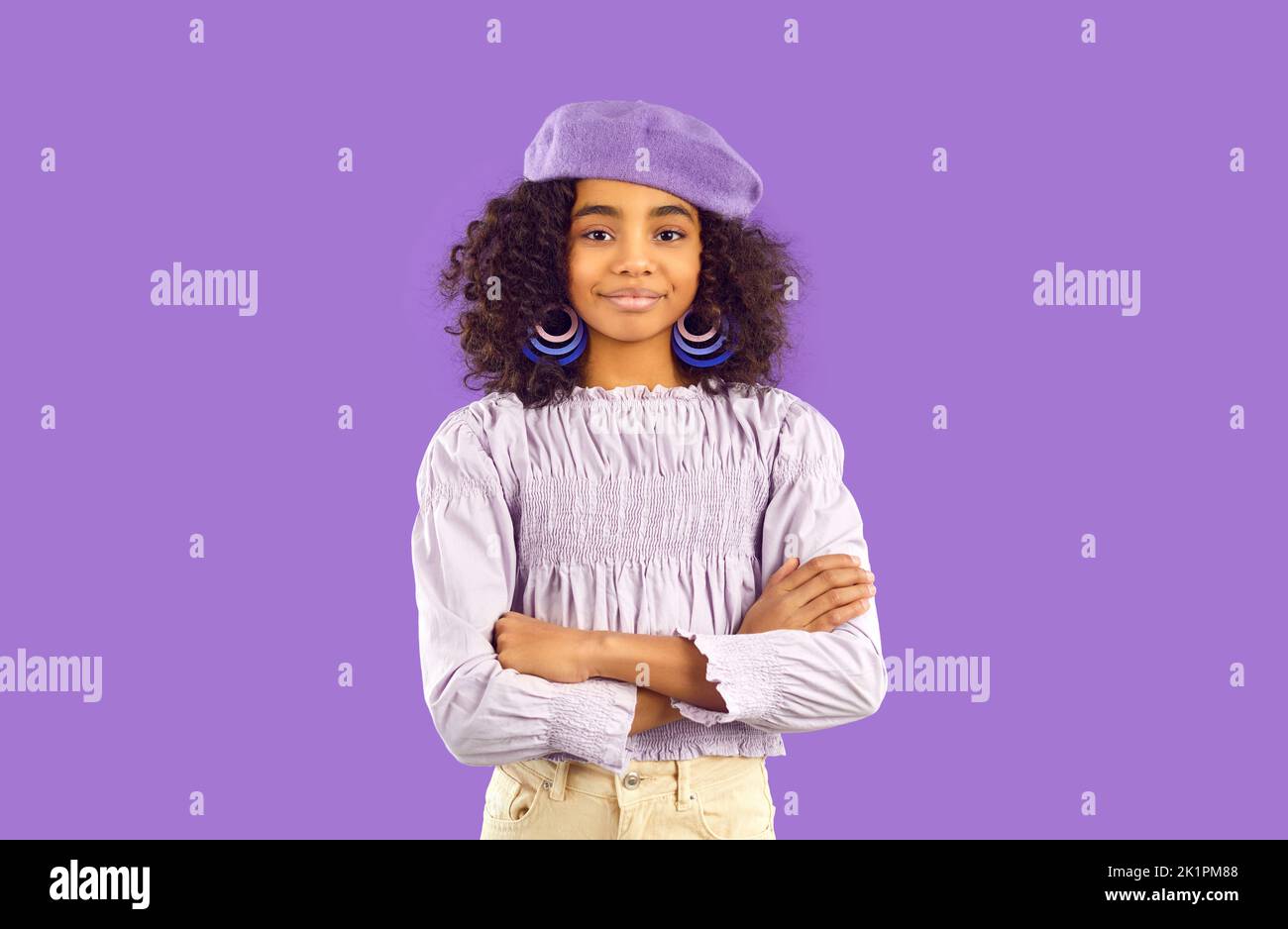 Happy pretty child in stylish top and beret hat standing on purple studio background Stock Photo