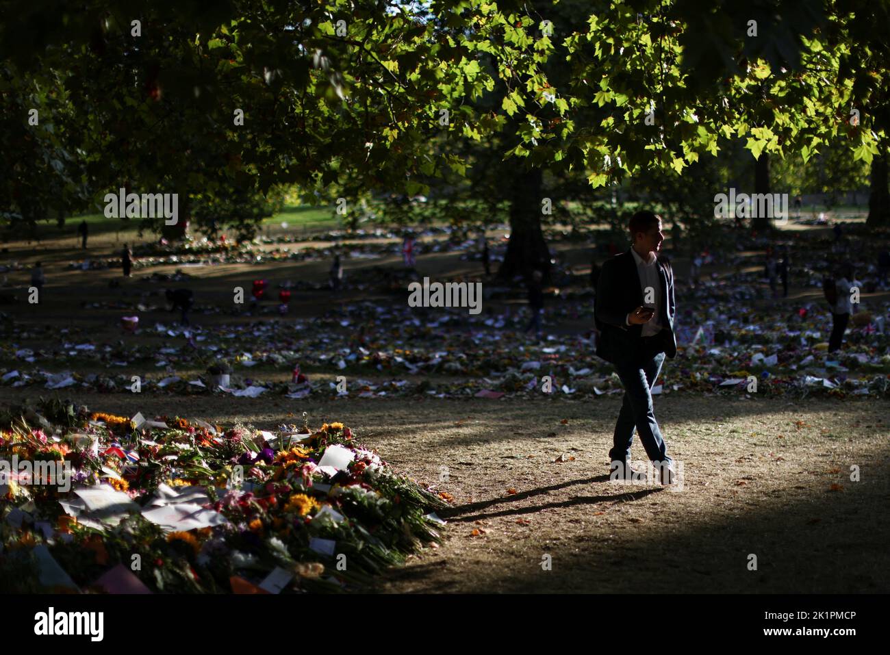 A man walks by as volunteers removes packaging from floral tributes, following the funeral of Britain's Queen Elizabeth, in Green Park in London, Britain September 20, 2022. REUTERS/Tom Nicholson Stock Photo