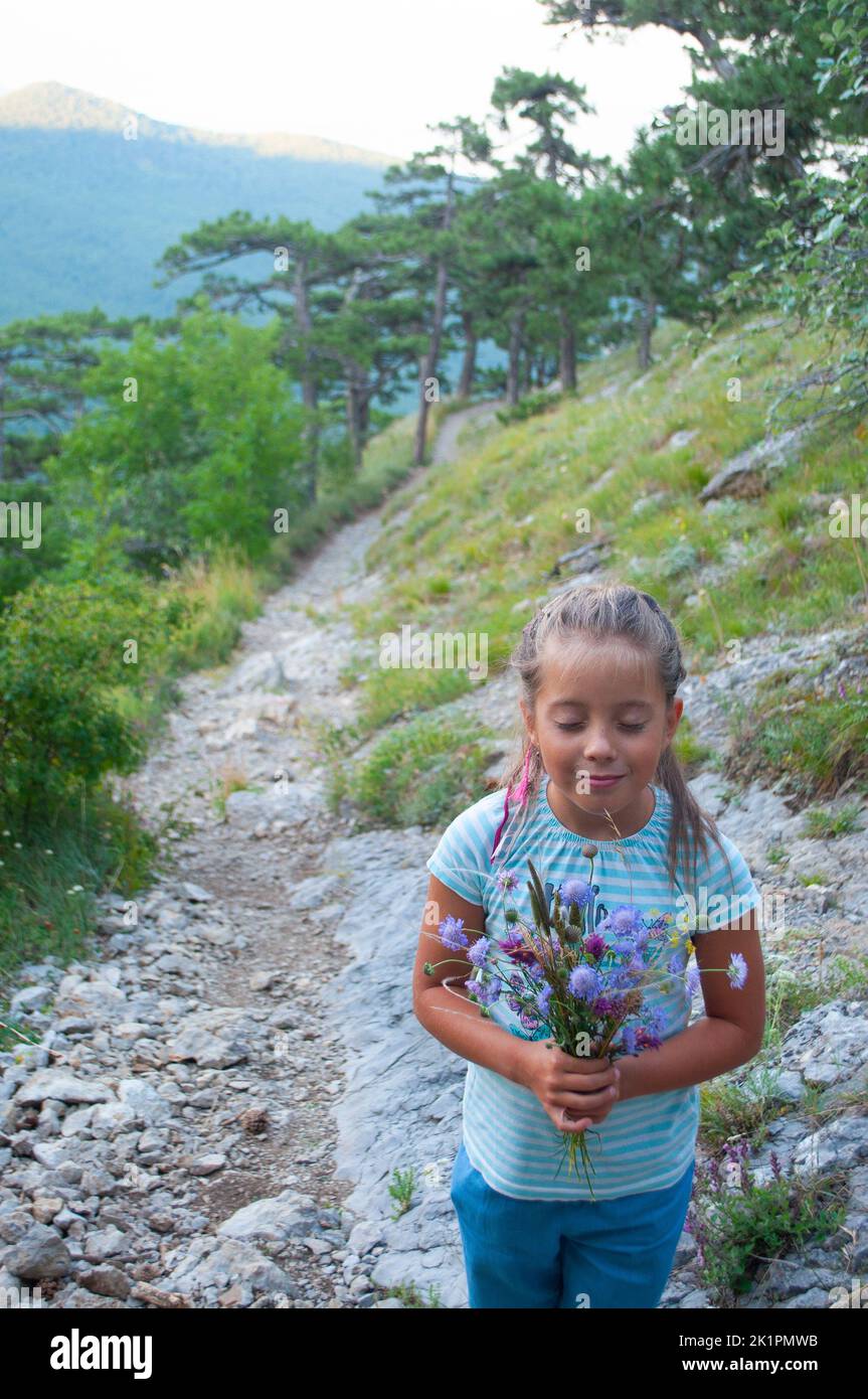 A happy little girl with a bouquet of wild flowers on a pathway in a forest. Stock Photo