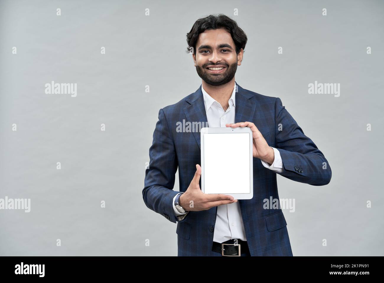 Smiling indian business manager wearing suit showing digital tablet mockup. Stock Photo