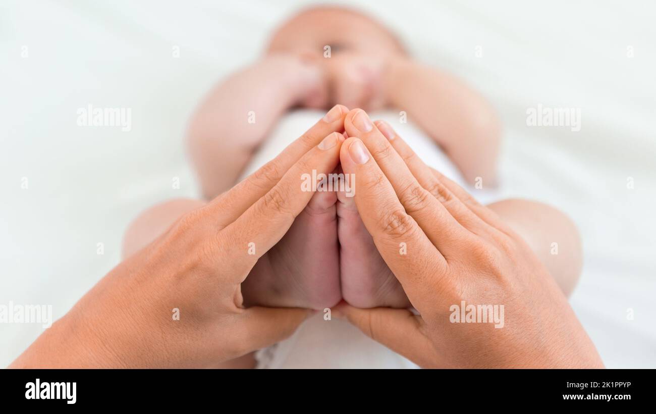 Mother is holding a foots of the newborn on a white sheet background. Mom squeezes a tiny foot of a baby boy. Family and home concept Stock Photo