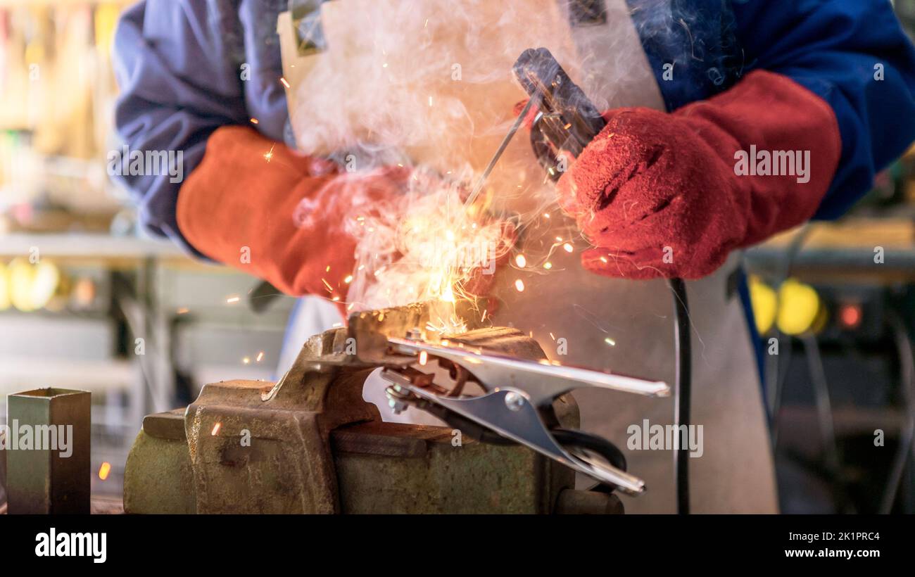 Skillful metal worker working with arc welding machine in factory while wearing safety equipment. Metalwork manufacturing and construction maintenance Stock Photo