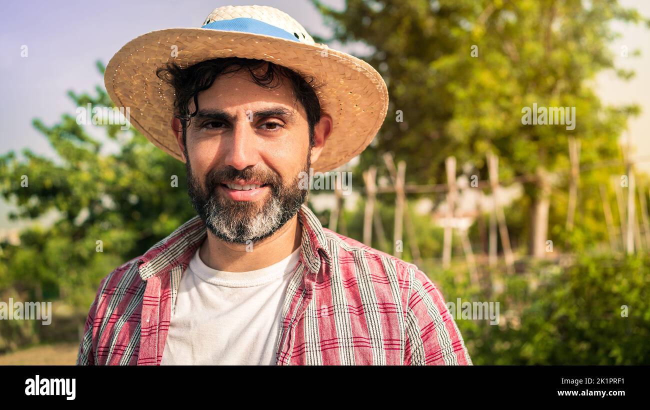 Portrait of a modern bearded farmer man looking at camera smile and stands in the agricultural field. Cheerful male worker in agricultural farm. Stock Photo
