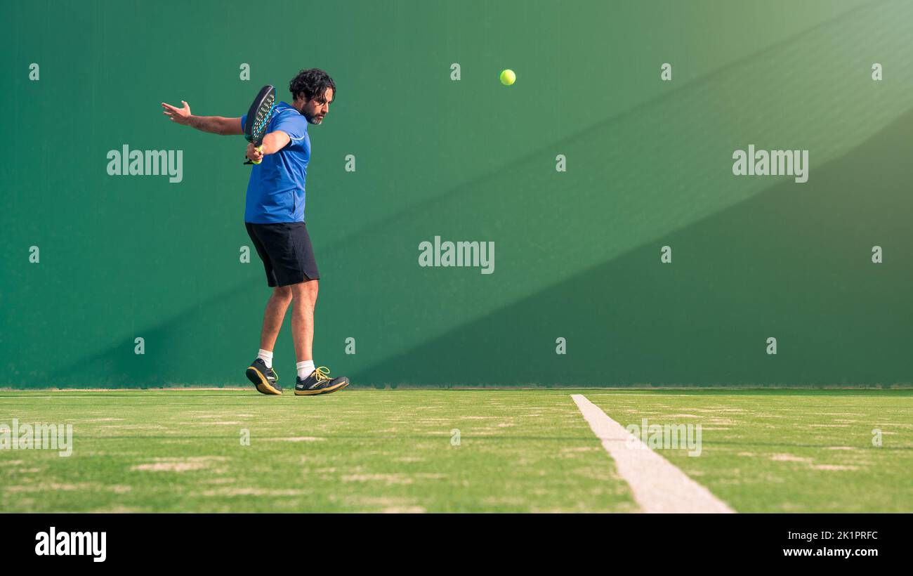 A padel player jump to the ball, good looking for posts and poster. Man with black racket playing a match in the open behind the net court outdoors. P Stock Photo