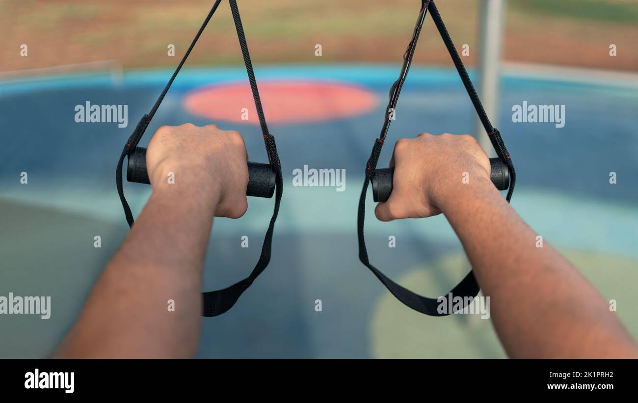 Close up hands of caucasian man during workout with suspension TRX on the street. Young active guy does suspension training with fitness straps outdoo Stock Photo