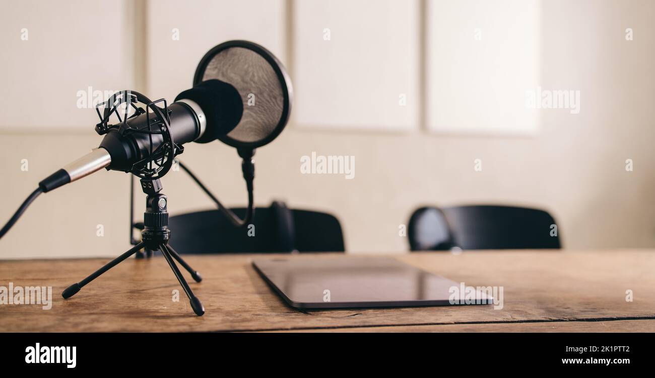 Still life shot of a microphone with a pop shield placed on a table alongside a digital tablet. Podcast recording equipment set in a home studio. Stock Photo