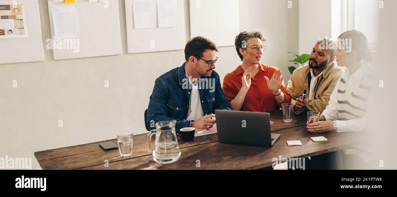 Group of creative businesspeople having a discussion using a laptop in a modern office. Diverse businesspeople sharing ideas while working together on Stock Photo