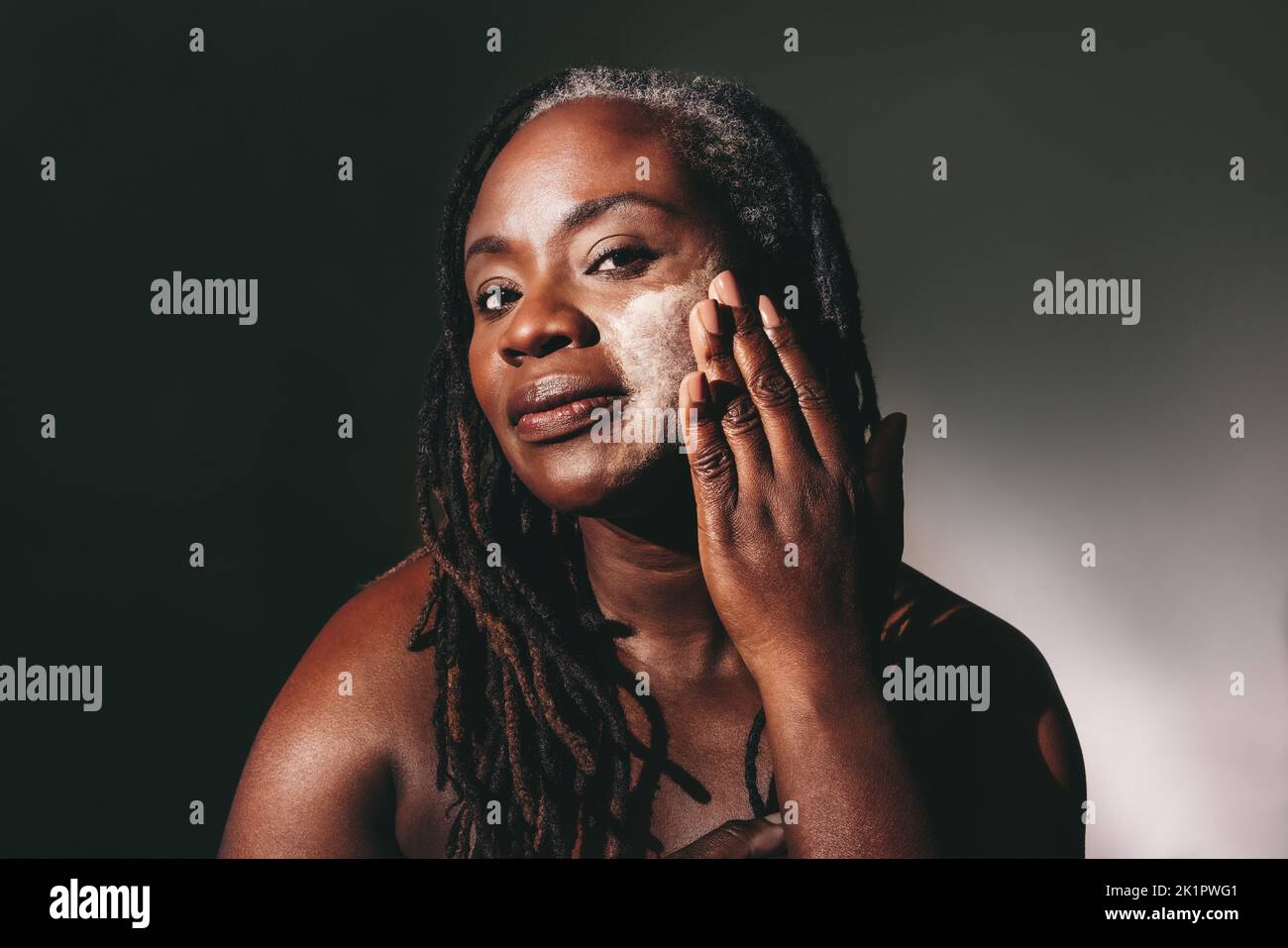 Woman with dreadlocks applying moisturizing cream on her face. Confident dark-skinned woman taking care of her flawless melanated skin. Mature black w Stock Photo