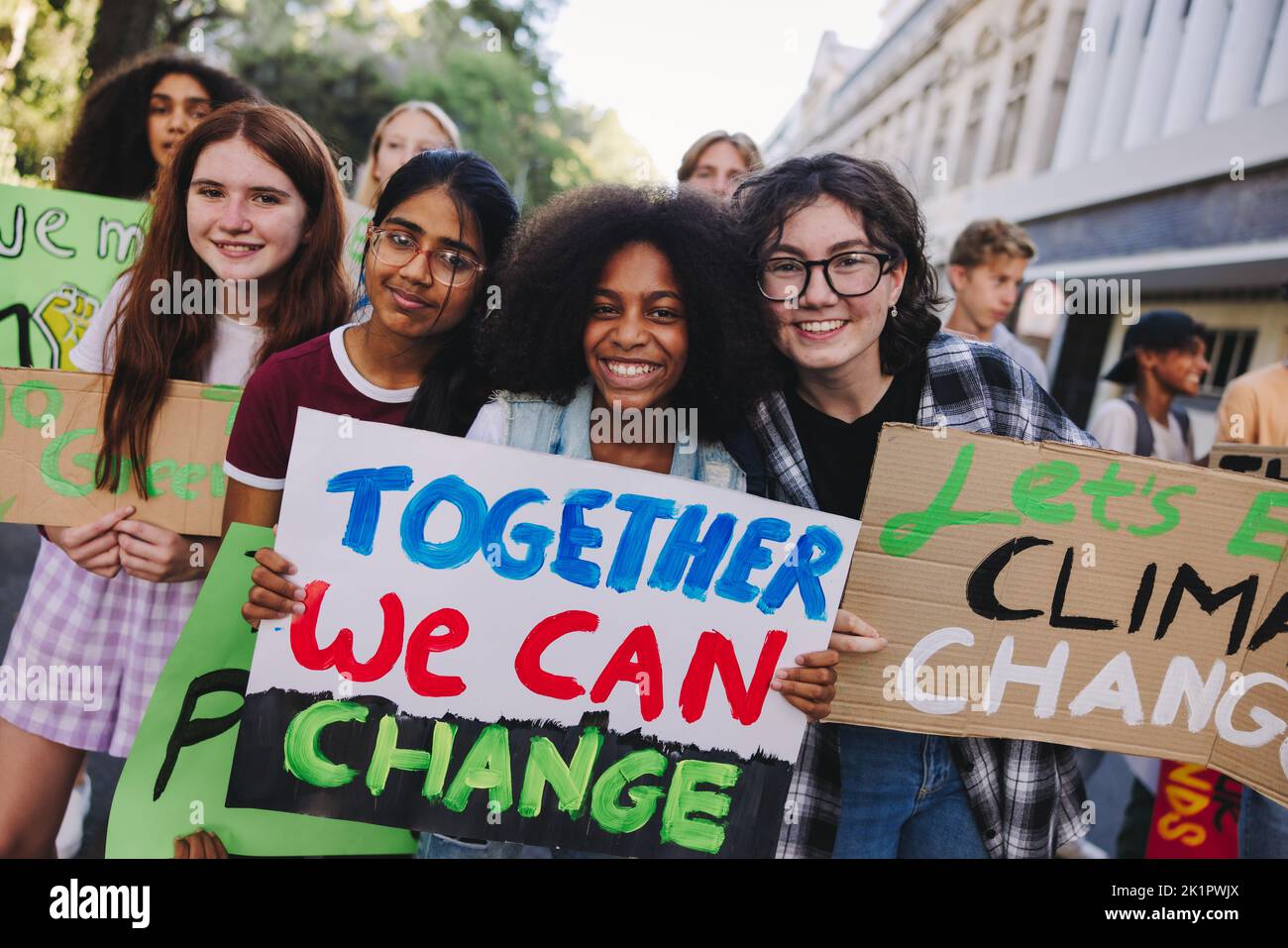 Happy teenage girls holding a posters during a climate change protest. Group of multicultural youth activists marching against global warming. Diverse Stock Photo