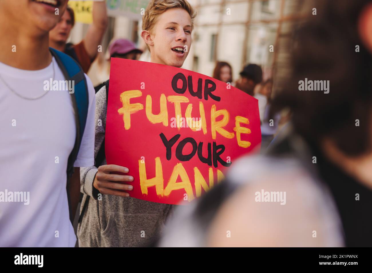 Teenage boy holding a poster while marching against climate change with a group of activists. Multicultural youth protestors campaigning for climate j Stock Photo