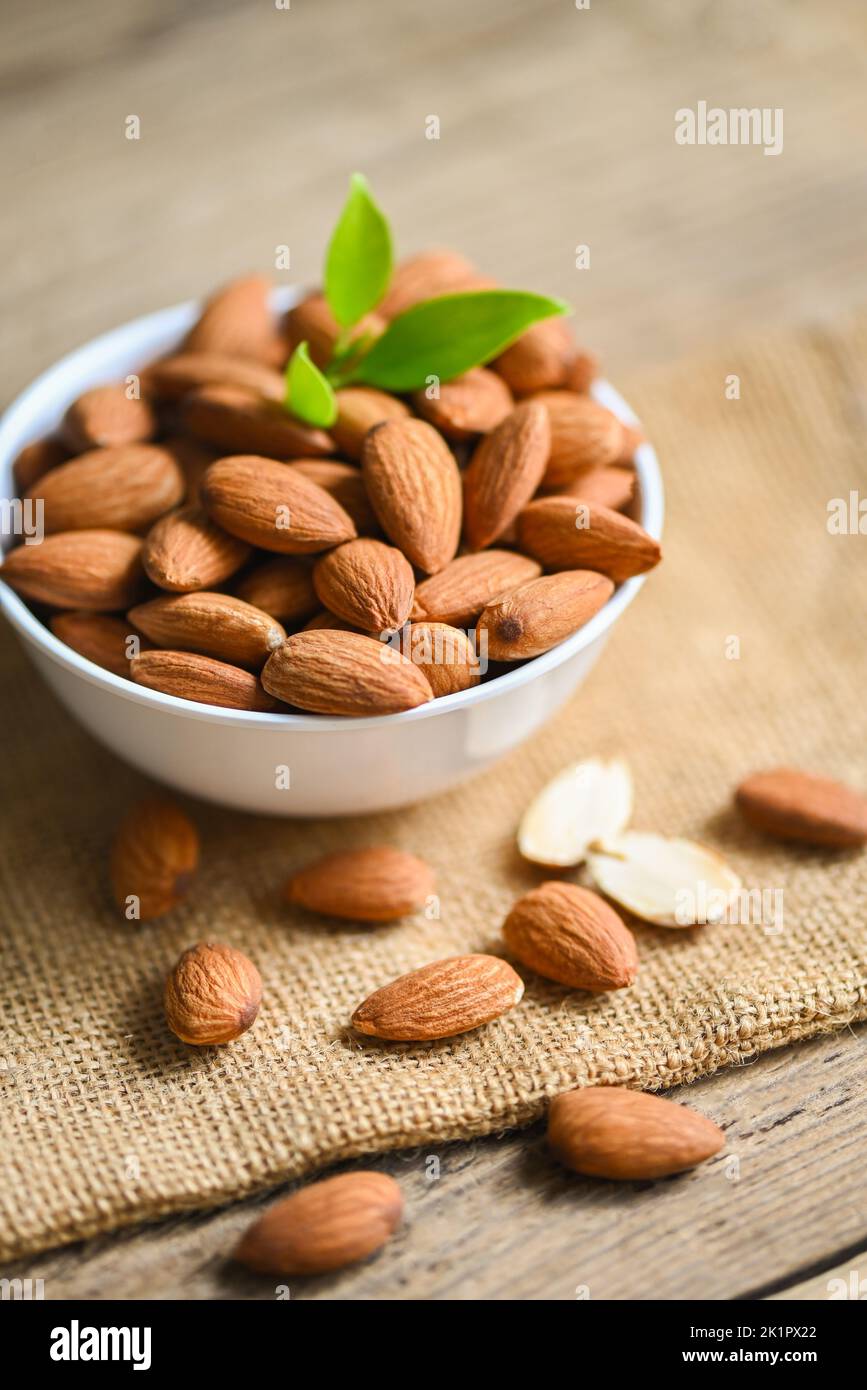 Delicious sweet almonds on the wooden table, roasted almond nut for healthy food and snack, Almonds nuts on white bowl and green leaf on sack backgrou Stock Photo