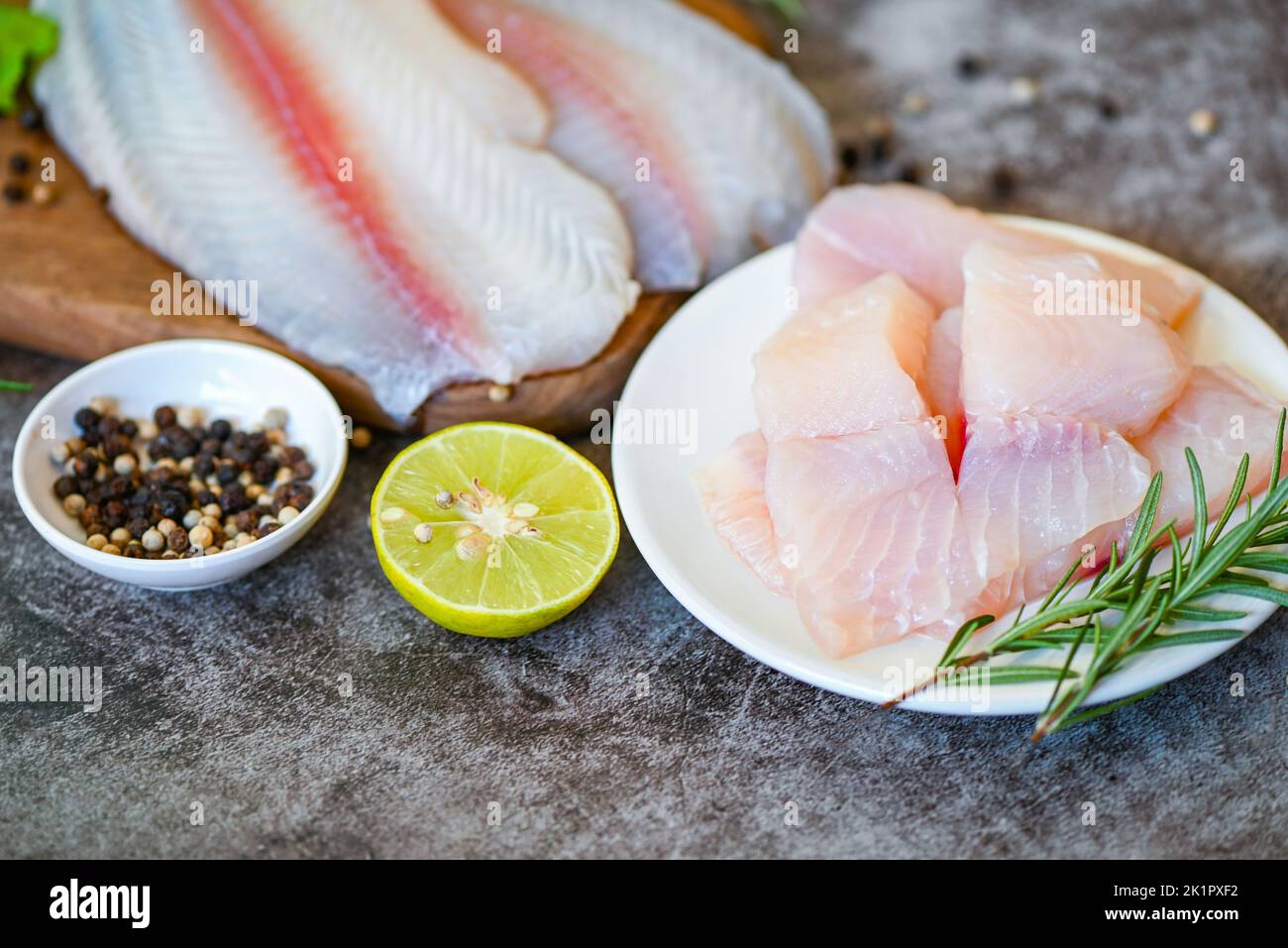 fresh raw pangasius fish fillet with herb and spices lemon lime and rosemary, meat dolly fish tilapia striped catfish, fish fillet on white plate with Stock Photo