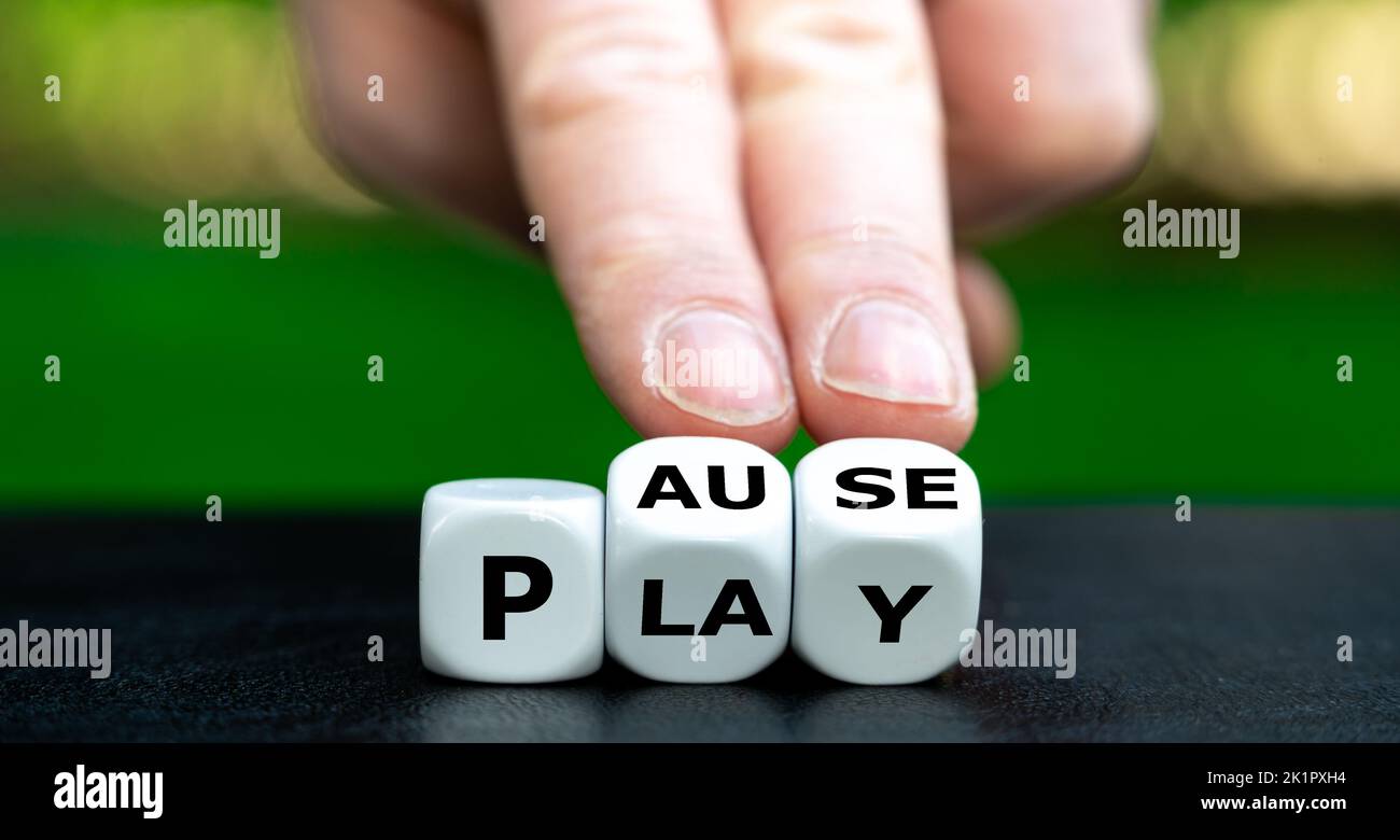 Hand turns dice and changes the word play to pause. Stock Photo
