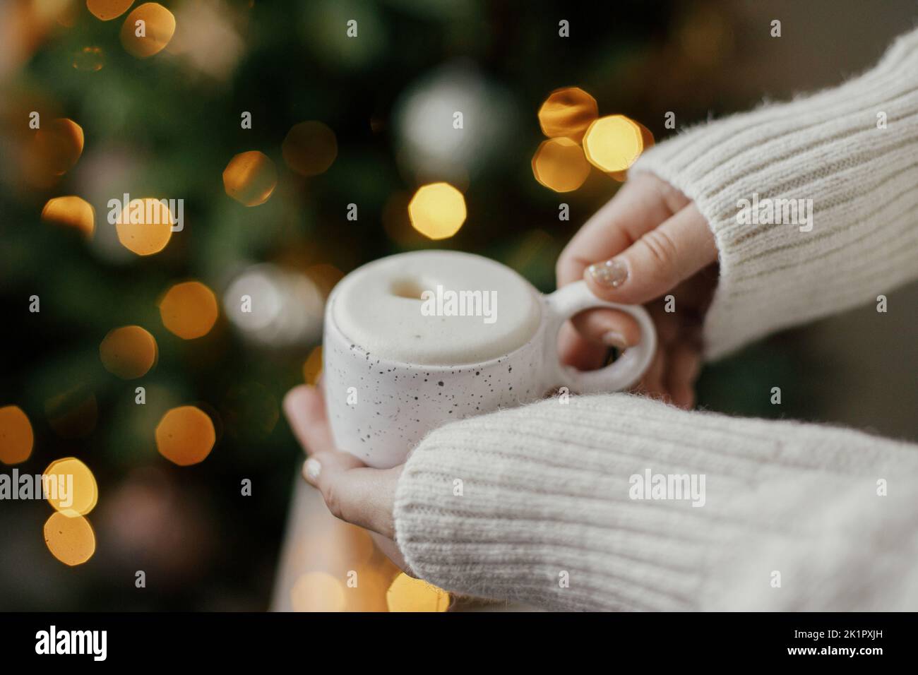 Hands holding warm cup of coffee on background of christmas tree with ...