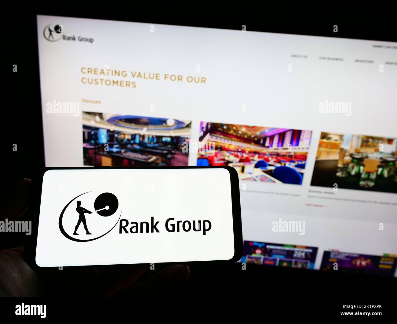 Person holding mobile phone with logo of British gambling company The Rank Group plc on screen in front of web page. Focus on phone display. Stock Photo