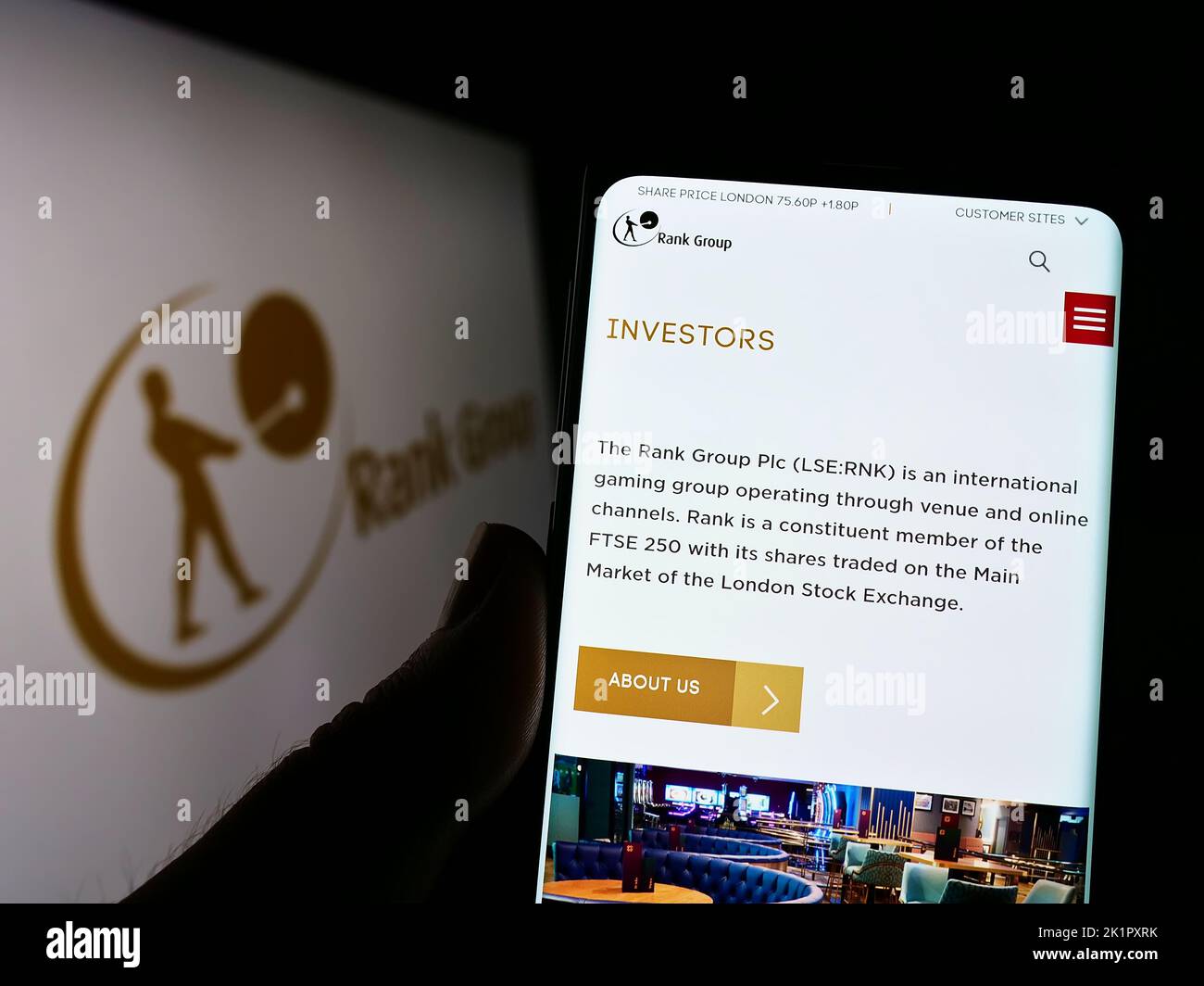 Person holding smartphone with webpage of British gambling company The Rank Group plc on screen in front of logo. Focus on center of phone display. Stock Photo