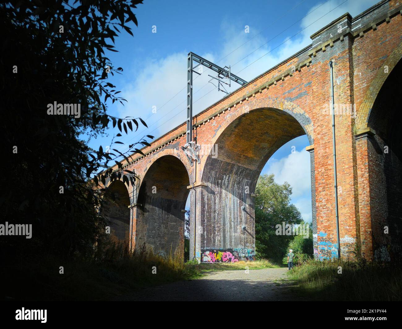 A man looks up at the arches of a victorian brick built railway viaduct, now electirified, in the countryside near Corby, England. Stock Photo