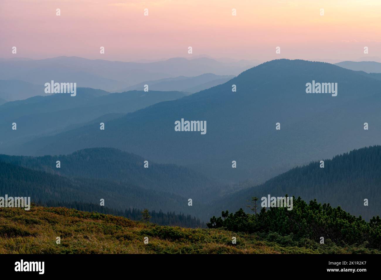 Beautiful tranquil evening high in the mountains. Pink alpine sunset with hazy mountain silhouettes Stock Photo