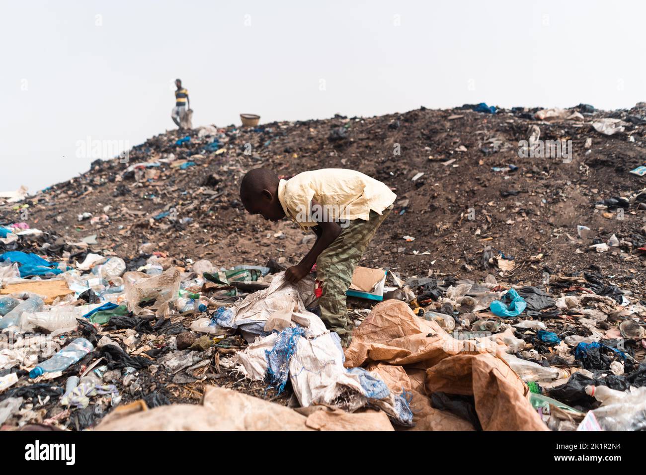 Small African boy busy recycling objects amidst heaps of plastic waste and dirt in an urban landfill; child labor concept Stock Photo