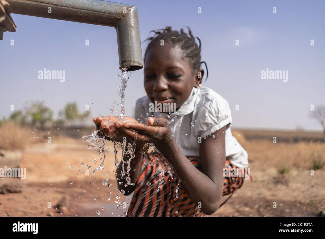 Close-up of an African girl collecting water from a village tap in an arid equatorial area; climate change concept Stock Photo