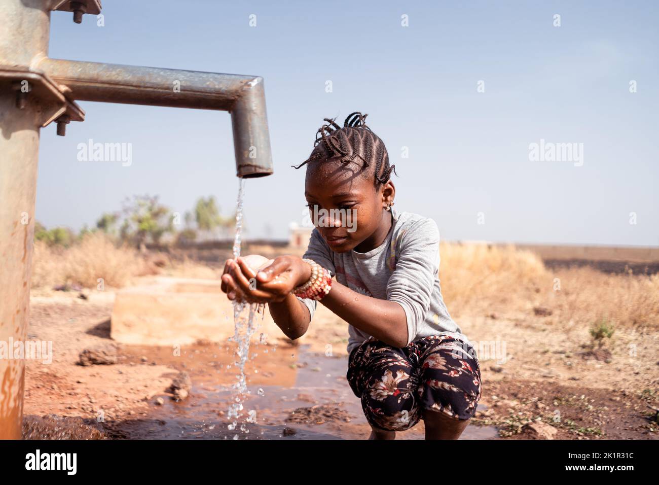 Smart little African girl kneeling in front of a tap collecting clean and fresh water; concept of lack of drinking water supply in rural areas Stock Photo