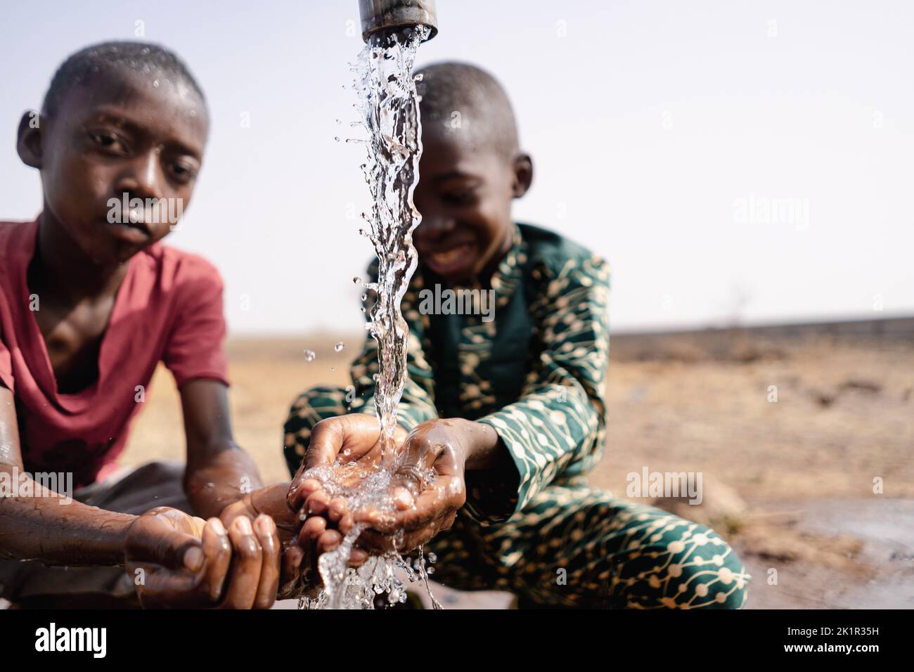 Two African toddlers playing with the water that flows from a rural faucet on the outskirts of their village; concept of water scarcity Stock Photo