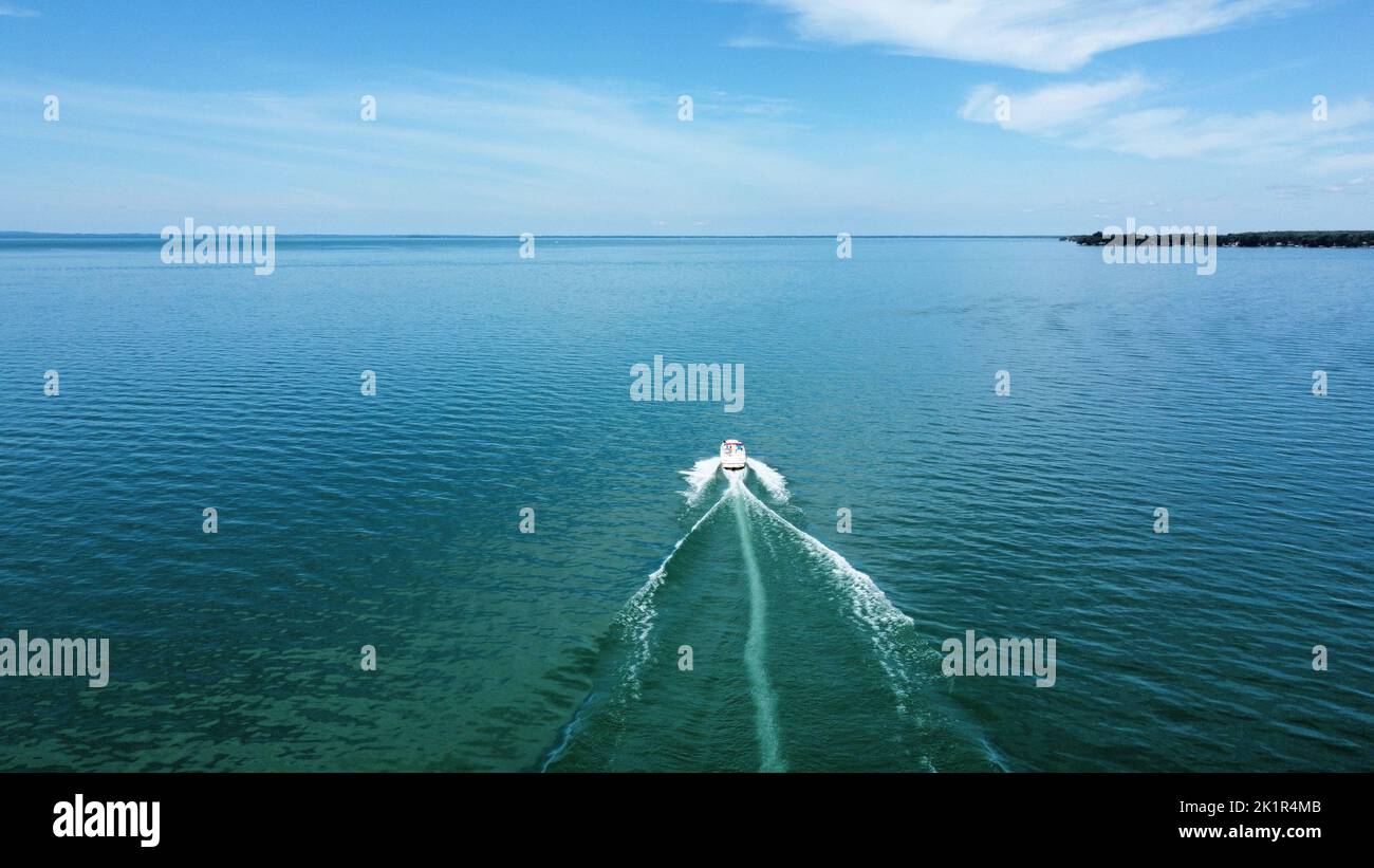A drone view of a motorboat driving on Lake Simcoe, Ontario with blue sky above Stock Photo