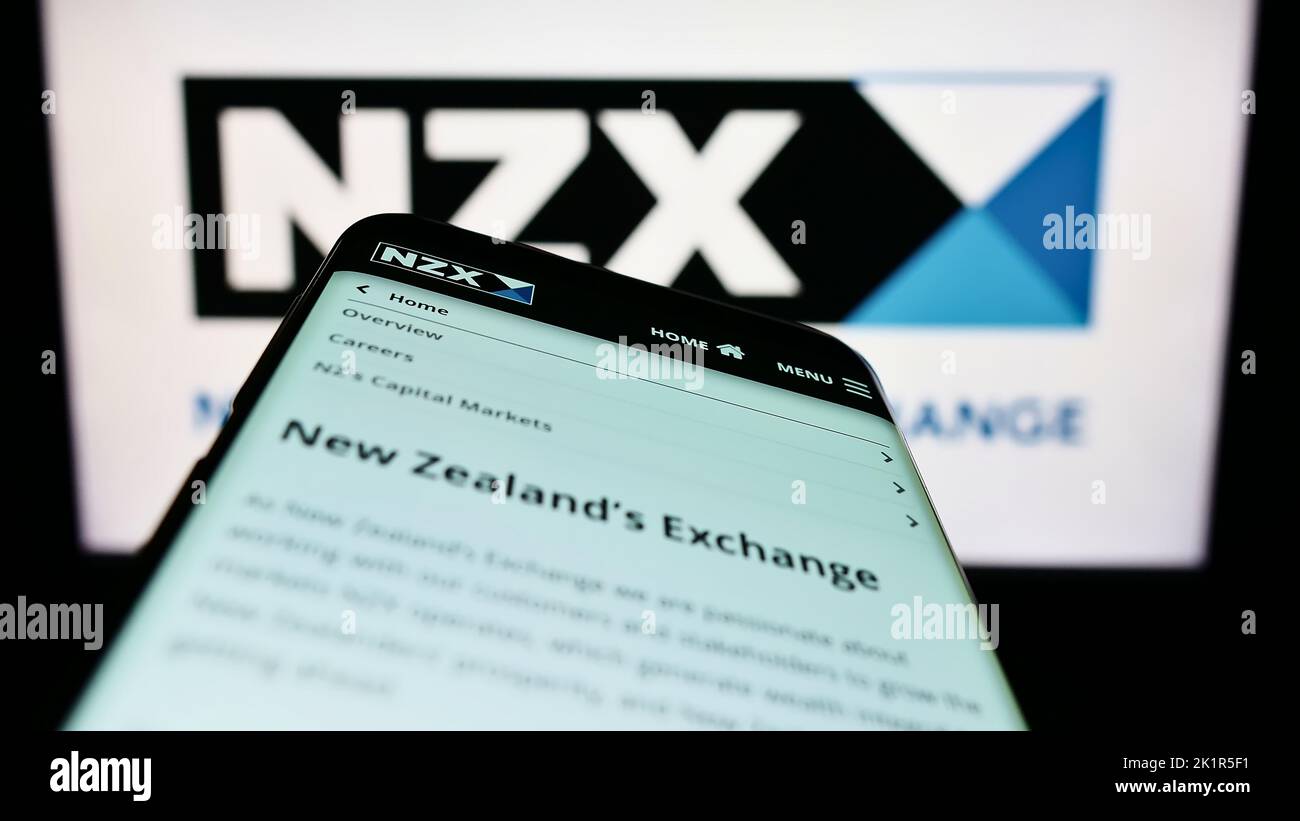 Smartphone with webpage of financial company New Zealand's Exchange (NZX) on screen in front of logo. Focus on top-left of phone display. Stock Photo