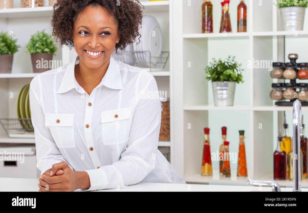 Beautiful happy biracial African American girl or young woman wearing a white shirt smiling with perfect teeth in her kitchen at home Stock Photo