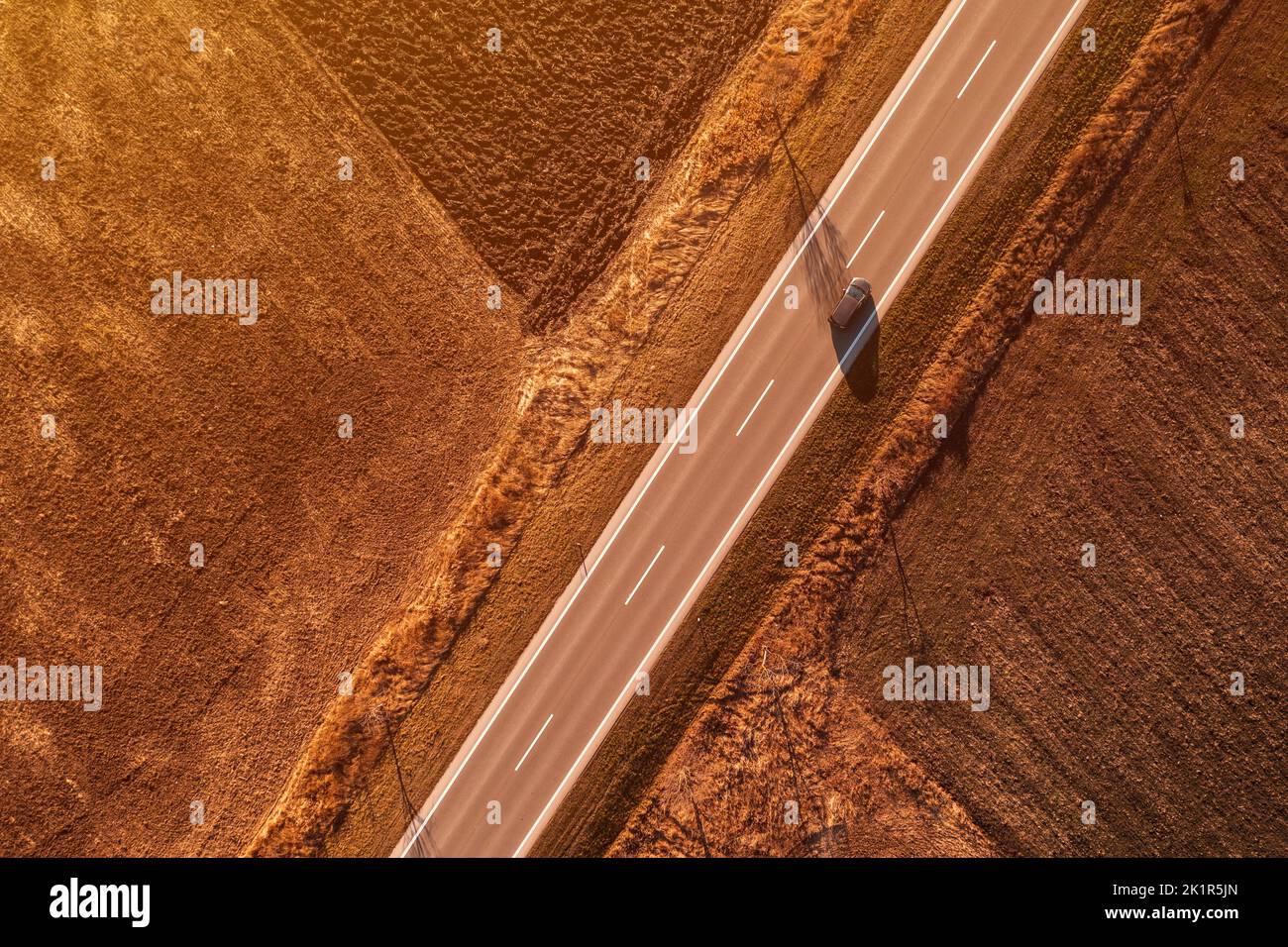 Dark passenger car driving along the highway in sunny autumn sunset, aerial shot from drone pov, directly above Stock Photo