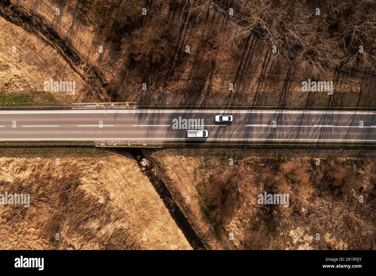 Aerial shot top view of car and truck on highway through autumn scenery landscape, drone pov directly above Stock Photo