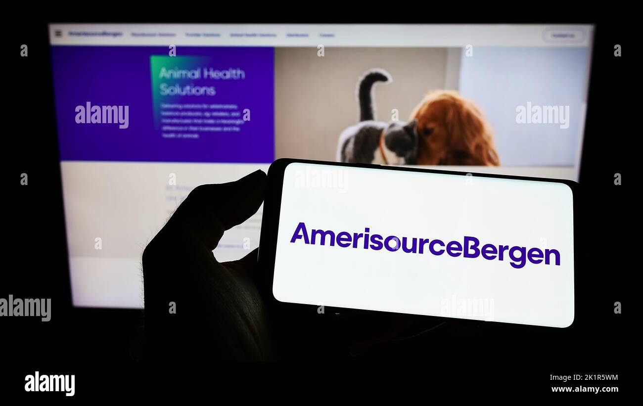 Person holding cellphone with logo of US drug company AmerisourceBergen Corporation on screen in front of web page. Focus on phone display. Stock Photo