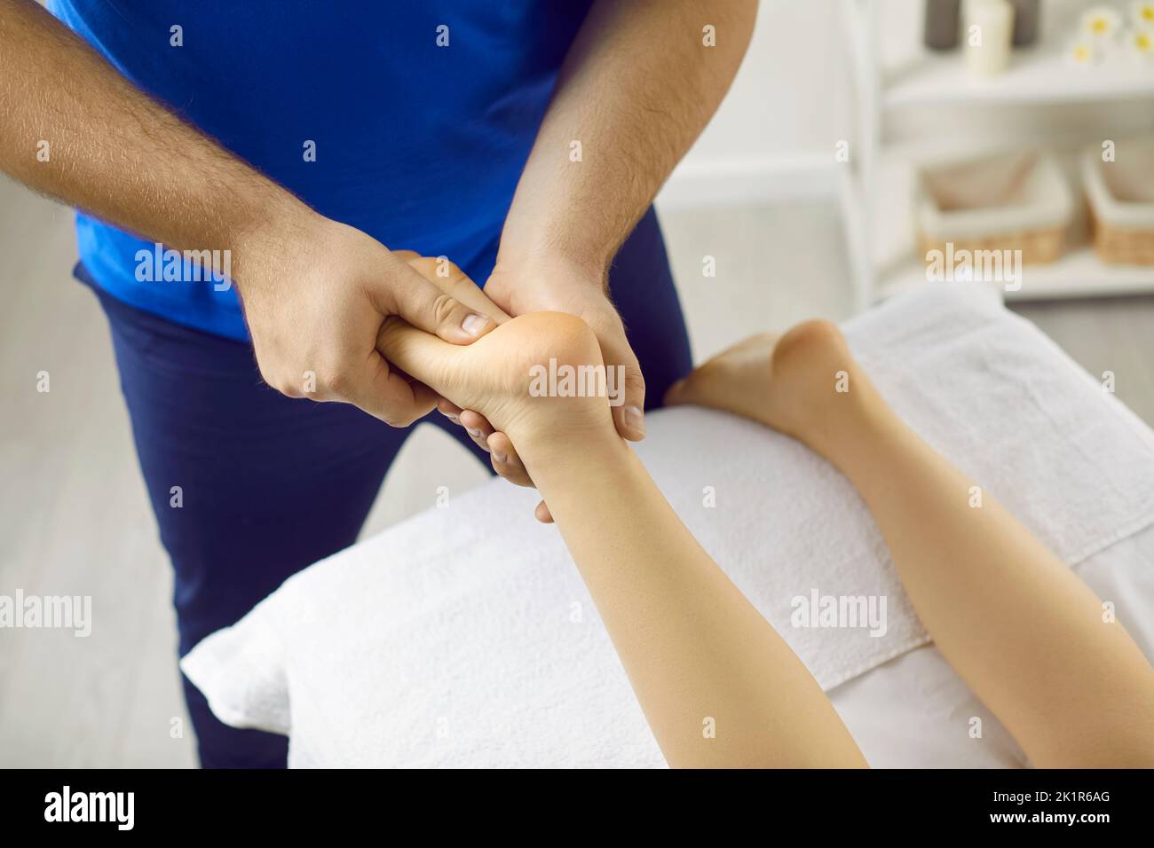 Male masseur with hands makes acupressure on legs of young woman in modern massage parlor. Stock Photo