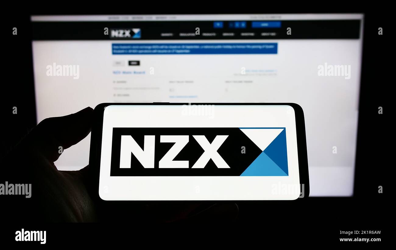 Person holding smartphone with logo of financial company New Zealand's Exchange (NZX) on screen in front of website. Focus on phone display. Stock Photo